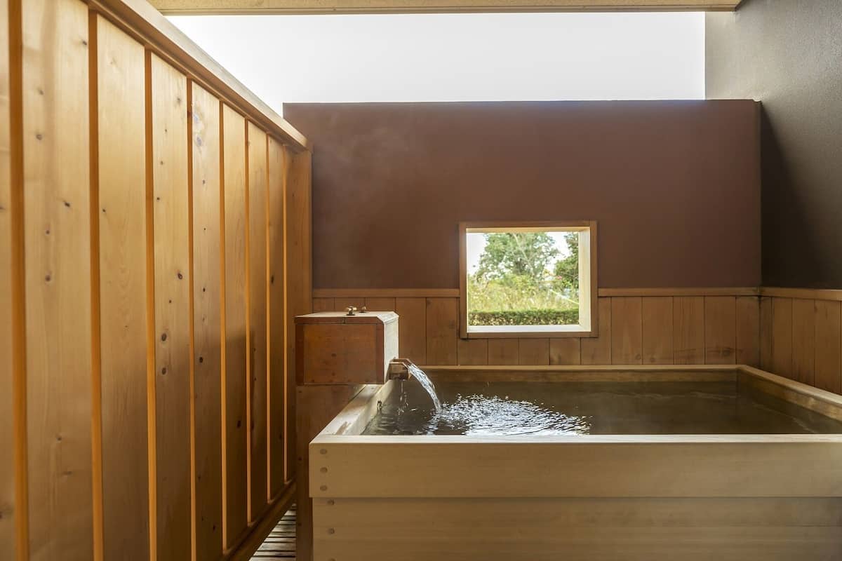 Een houten sauna met een raam, een houten bank en een waterspuit.