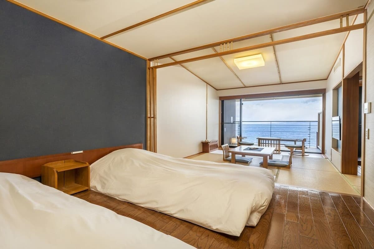 A hotel room with two beds, a wooden floor, a view of the sea, and a balcony area with seating.