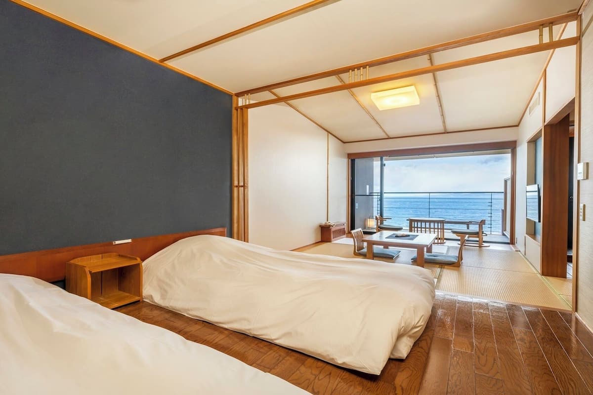 Een kamer met twee bedden, een klein houten nachtkastje en een balkon met uitzicht op zee.