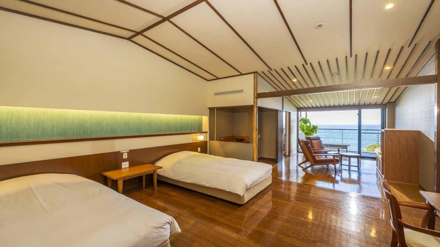 Ein Hotelzimmer mit zwei Betten, Holzboden, Meerblick und einem Balkon mit Sitzgelegenheit.