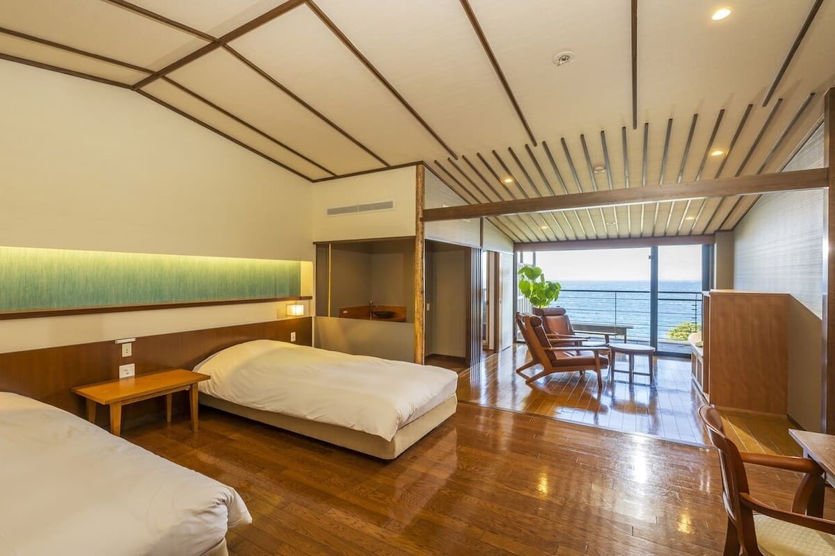 Een hotelkamer met twee bedden, een houten vloer, uitzicht op zee en een balkon met zitplaatsen.