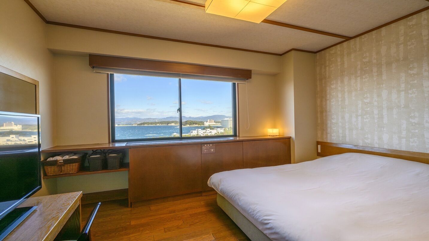 Ein Hotelzimmer mit Bett, Schreibtisch, Fenster mit Meerblick und Nachttisch.
