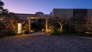 A paved entrance pathway leading to a building with a wooden archway and a modern building in the background. - Hamadachidori no Yu Kaishu (Shirahama)