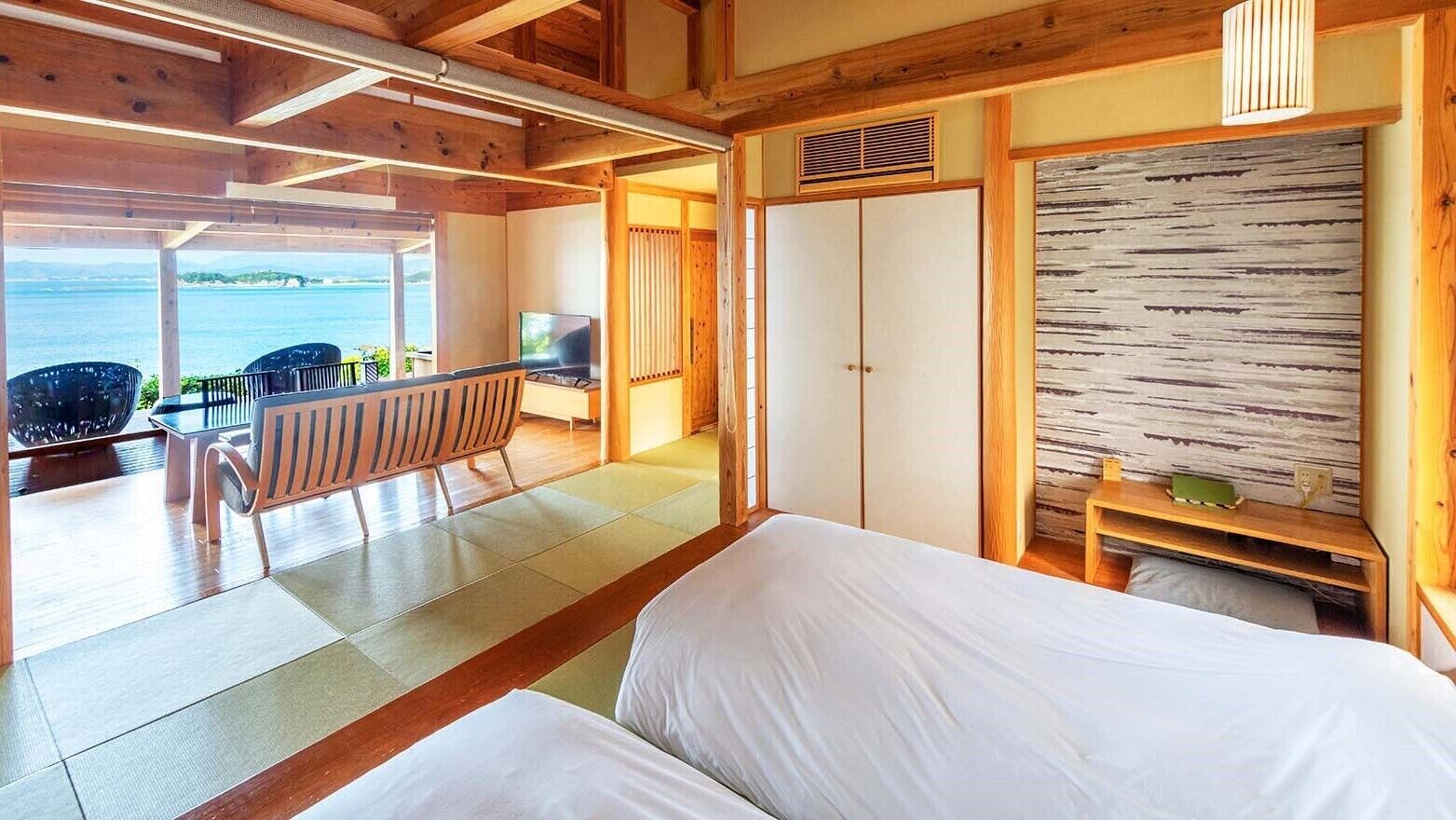 Ein Zimmer mit einem Bett, einem Fernseher, einer hölzernen Bank und Meerblick.