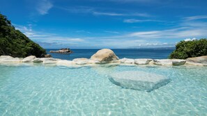 A clear pool with rocks and a view of the ocean.