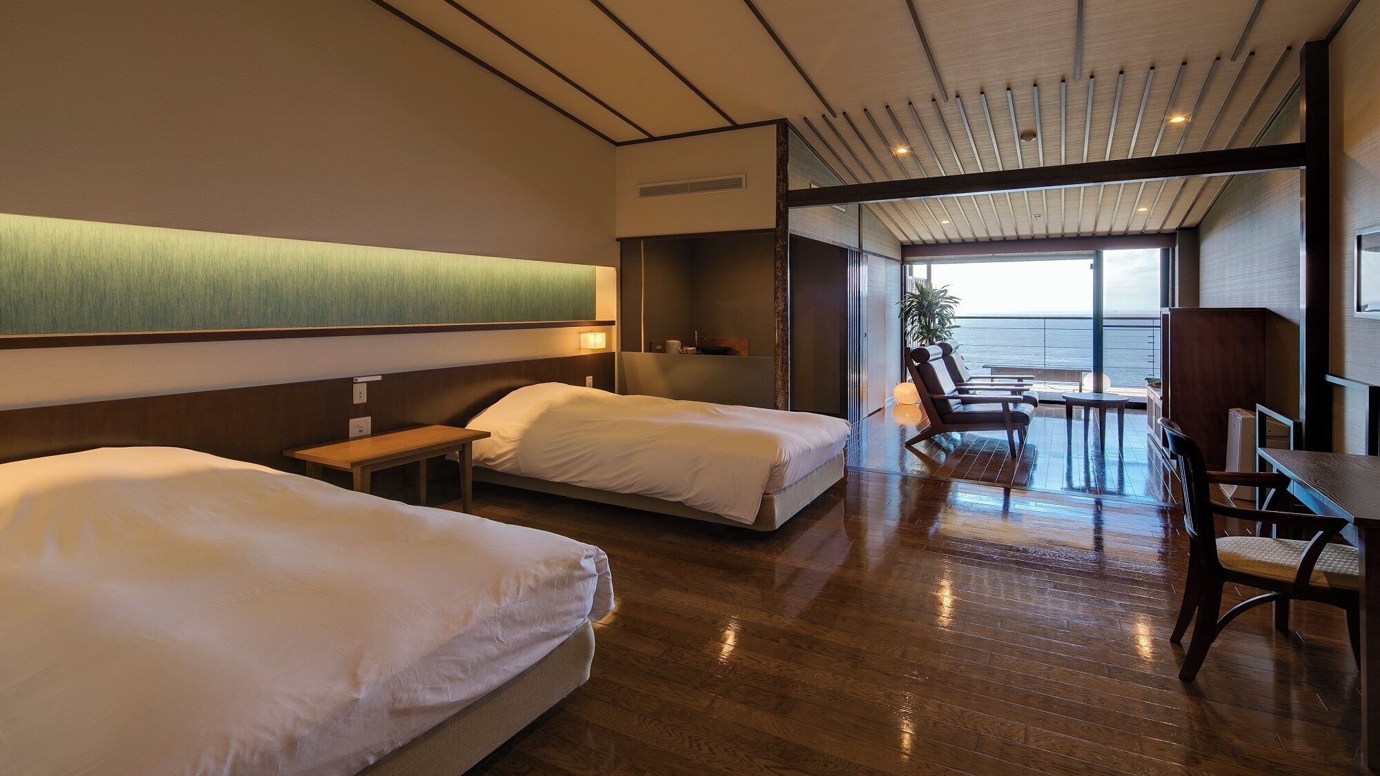 Ein Hotelzimmer mit zwei Betten, einem kleinen Tisch, einem Stuhl und Blick auf den Ozean.