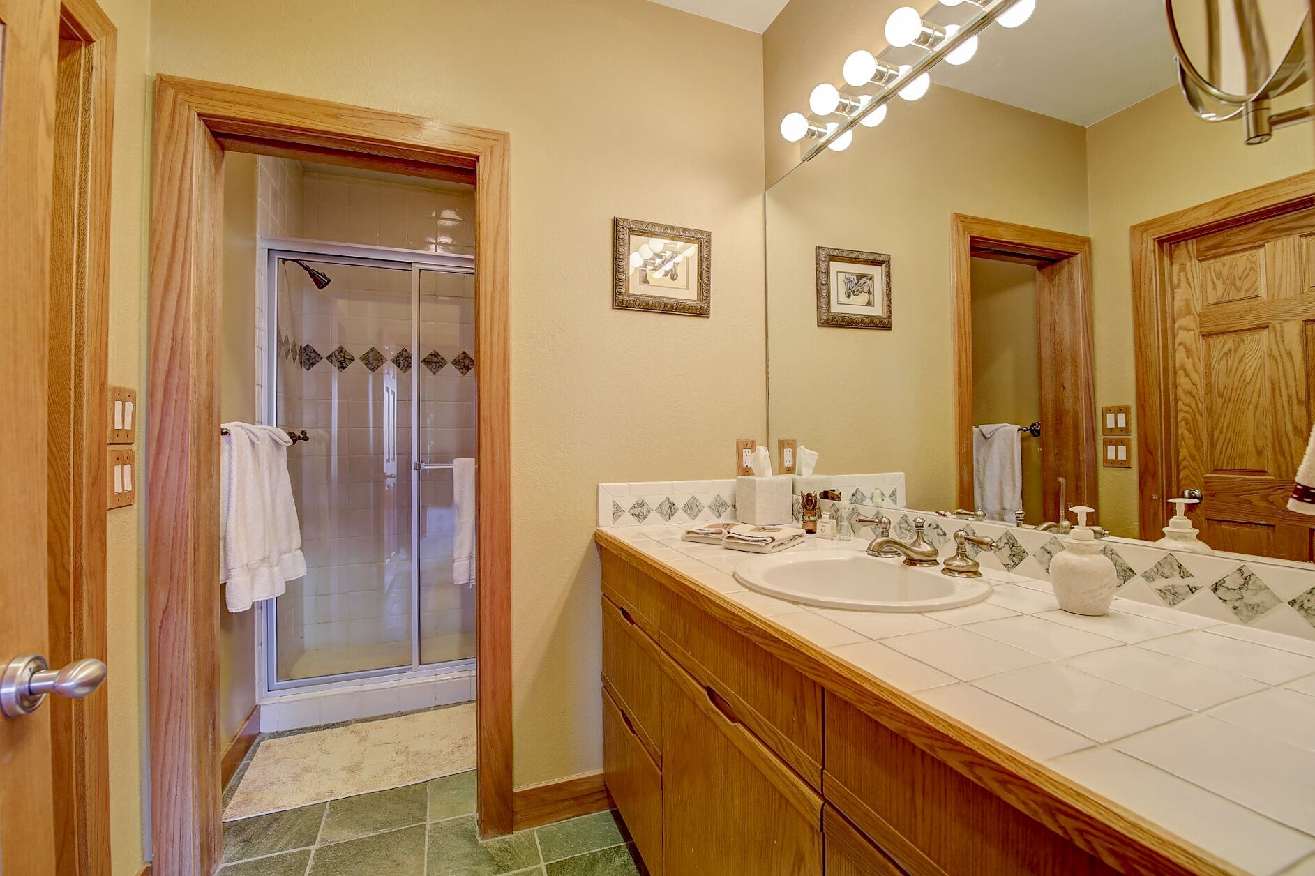 Une salle de bain avec une douche en verre, un meuble-lavabo en bois et un grand miroir avec des lumières au-dessus.