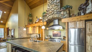 A spacious kitchen with a large island, wooden cabinets, a stone accent wall, and a stainless steel refrigerator.