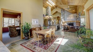 A spacious living area with a large wooden dining table, multiple chairs, and a stone fireplace.
