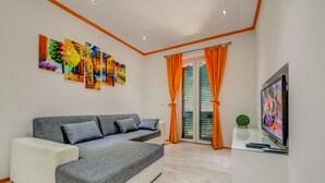 A modern living room with a grey sectional sofa, a flat-screen TV, and colorful artwork on the wall. - Split Suites Centre Apartman Anka (Split)