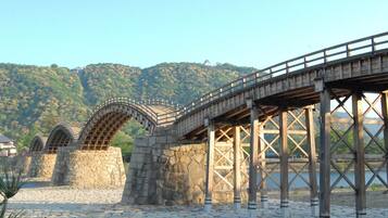 A stone bridge with a wooden walkway, set against a backdrop of green hills and a clear sky.