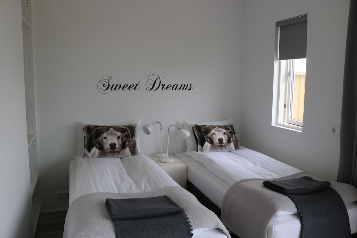 A bedroom with two beds, each with a pillow featuring a dog. There is a wall-mounted sign that reads "Sweet Dreams."