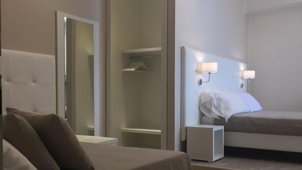 A modern hotel room with a large bed, a bedside table, a nightstand, a mirror, and a walk-in closet.