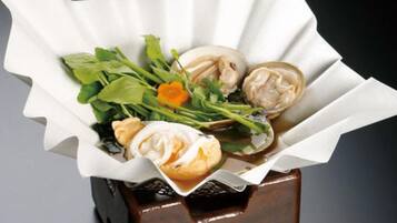 A dish with clams and greens in a paper-lined container.