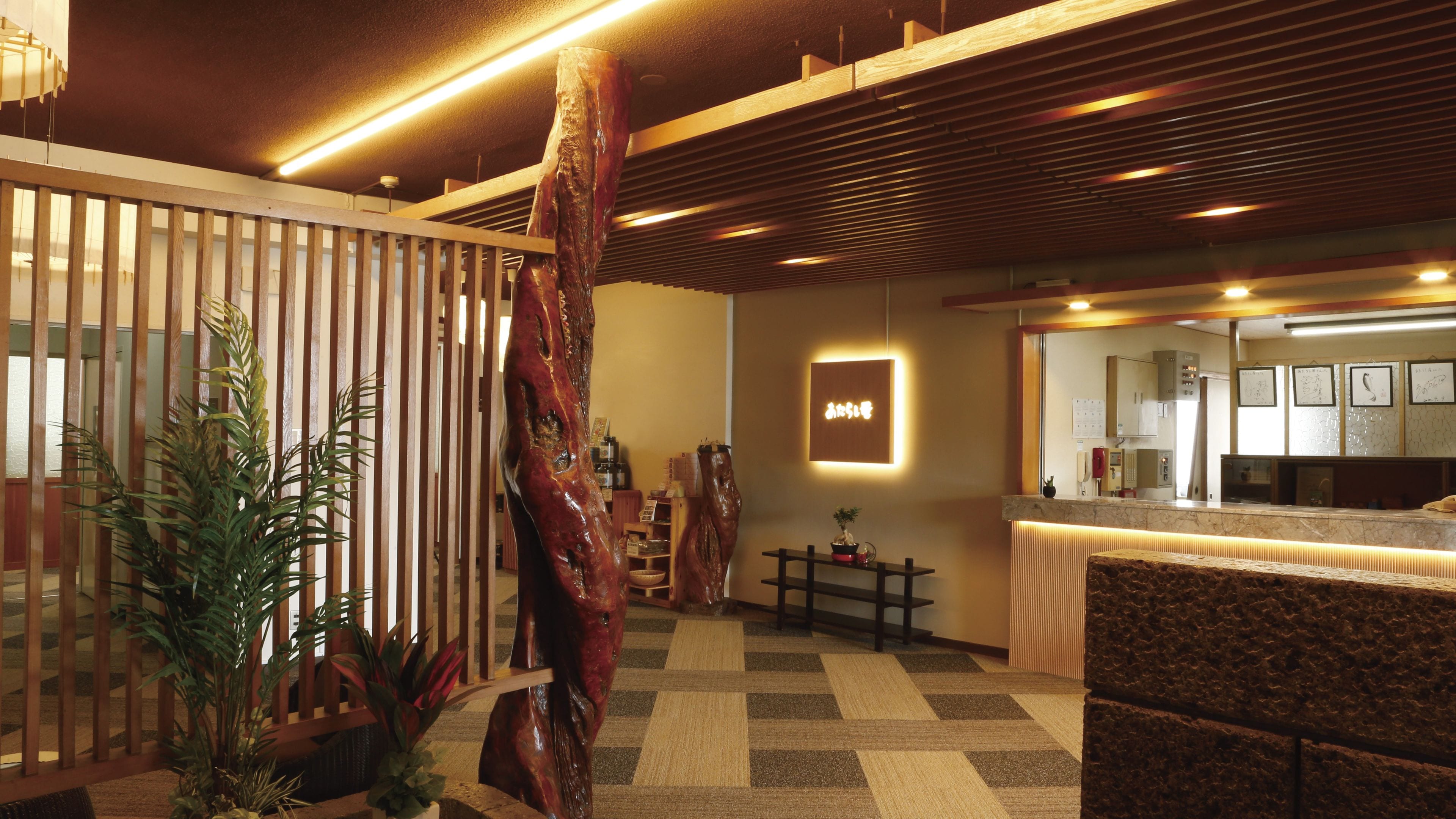 A reception area with a wooden reception desk, a large plant, and a wall-mounted sign.