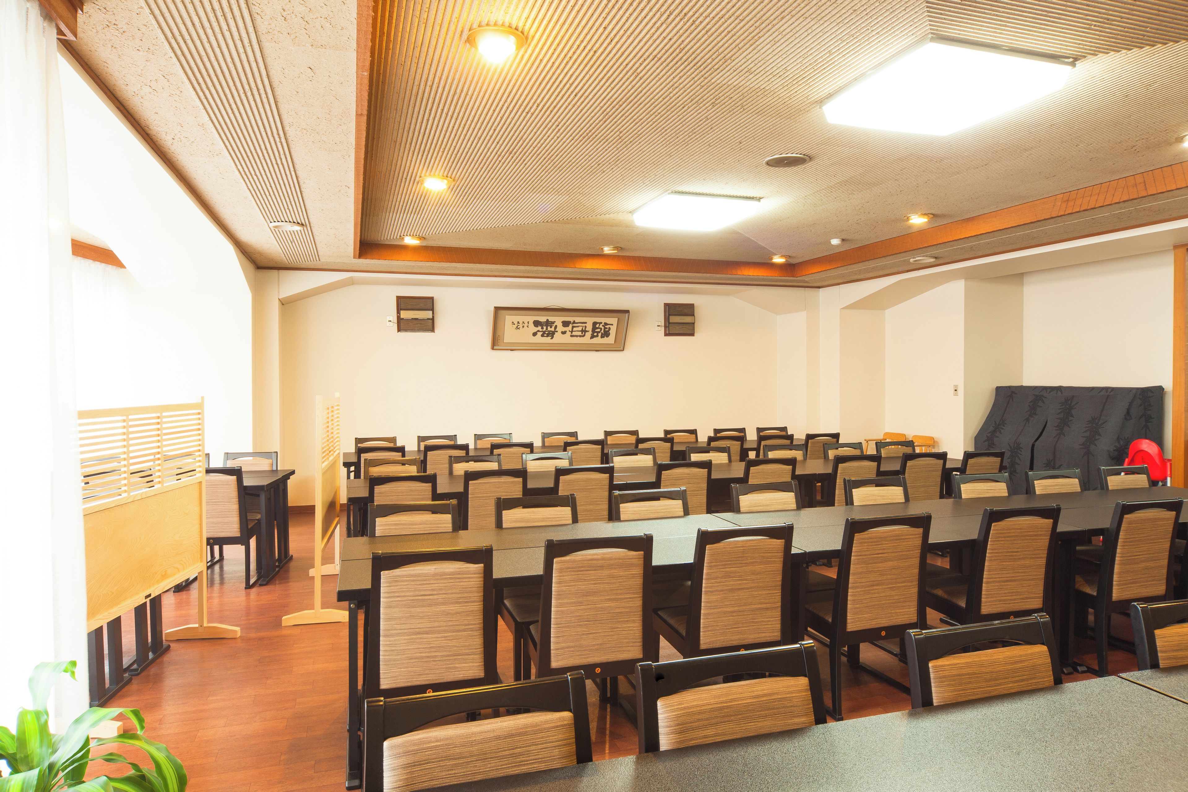 Un salón de conferencias con filas de mesas y sillas, techo de madera y un cartel enmarcado en la pared.