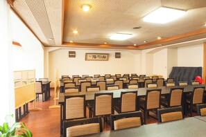 Une salle de conférence avec des rangées de tables et de chaises, un plafond en bois et un panneau encadré accroché au mur.