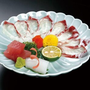 Une assiette contenant des sashimis, du wasabi, du gingembre mariné et une tranche de citron vert.