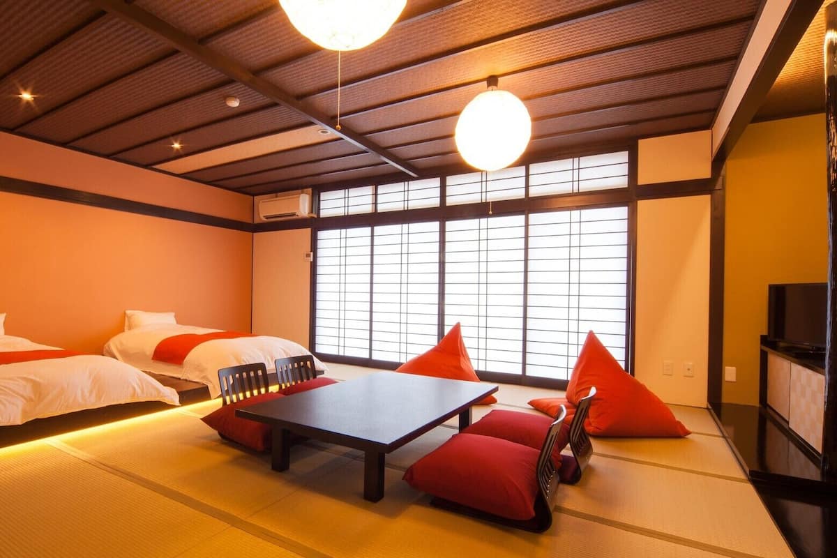 Una habitación tradicional japonesa con suelo de tatami, dos camas, una mesita baja y cojines rojos.