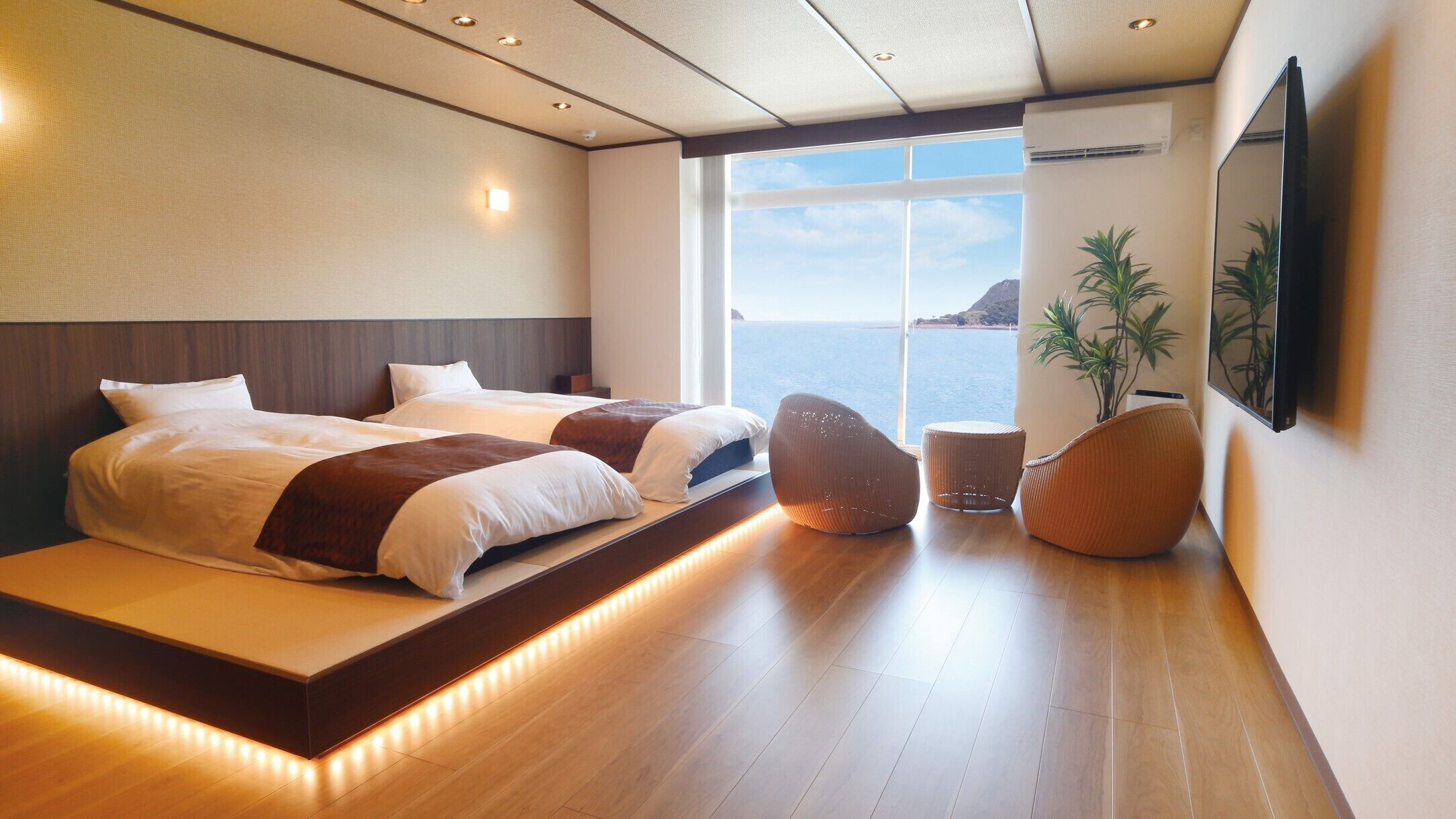 Habitación de hotel moderna con una cama grande, zona de estar, una planta y vista al mar.