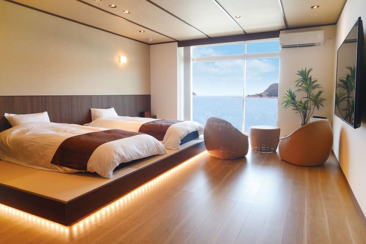 Habitación de hotel moderna con una cama grande, zona de estar, una planta y vista al mar.