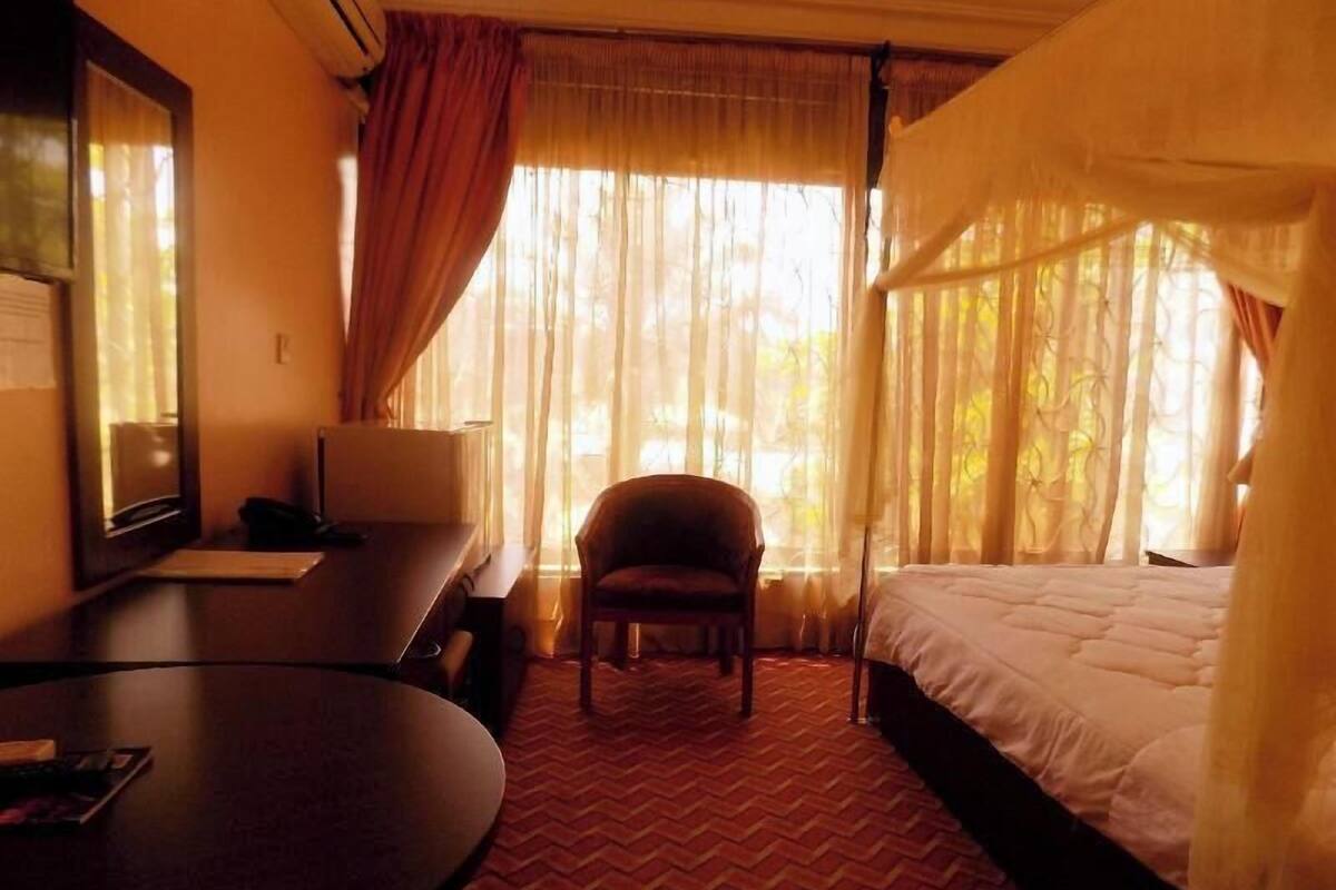 Ein Hotelzimmer mit Bett, Sessel, Schreibtisch und einem Fenster mit Vorhängen.
