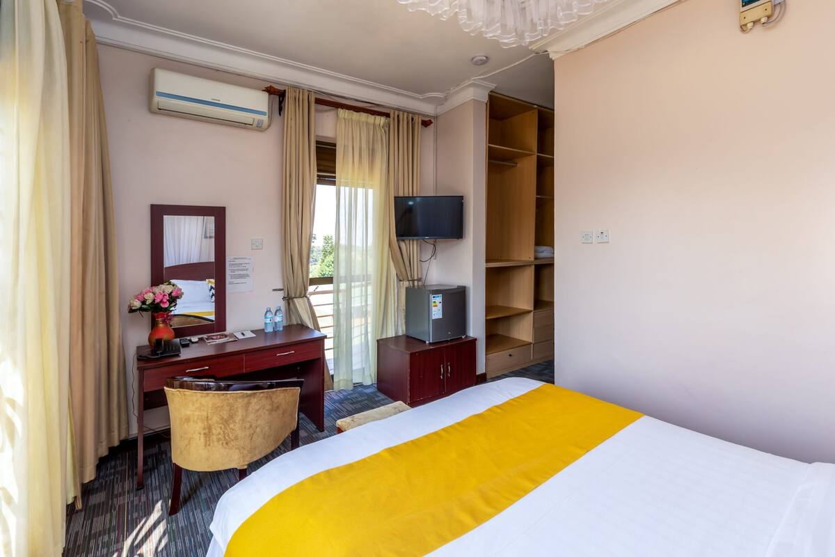 Ein Hotelzimmer mit Bett, Schreibtisch, Stuhl, Fernseher, Klimaanlage und Kleiderschrank.
