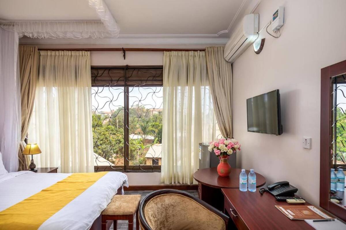 Ein Hotelzimmer mit Bett, Schreibtisch mit Stuhl, Fernseher und einem Fenster mit Vorhängen.
