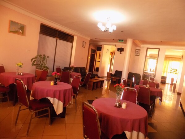 Un comedor con mesas redondas cubiertas de manteles rojos, rodeado de sillas rojas. Hay plantas en macetas y velas sobre las mesas.