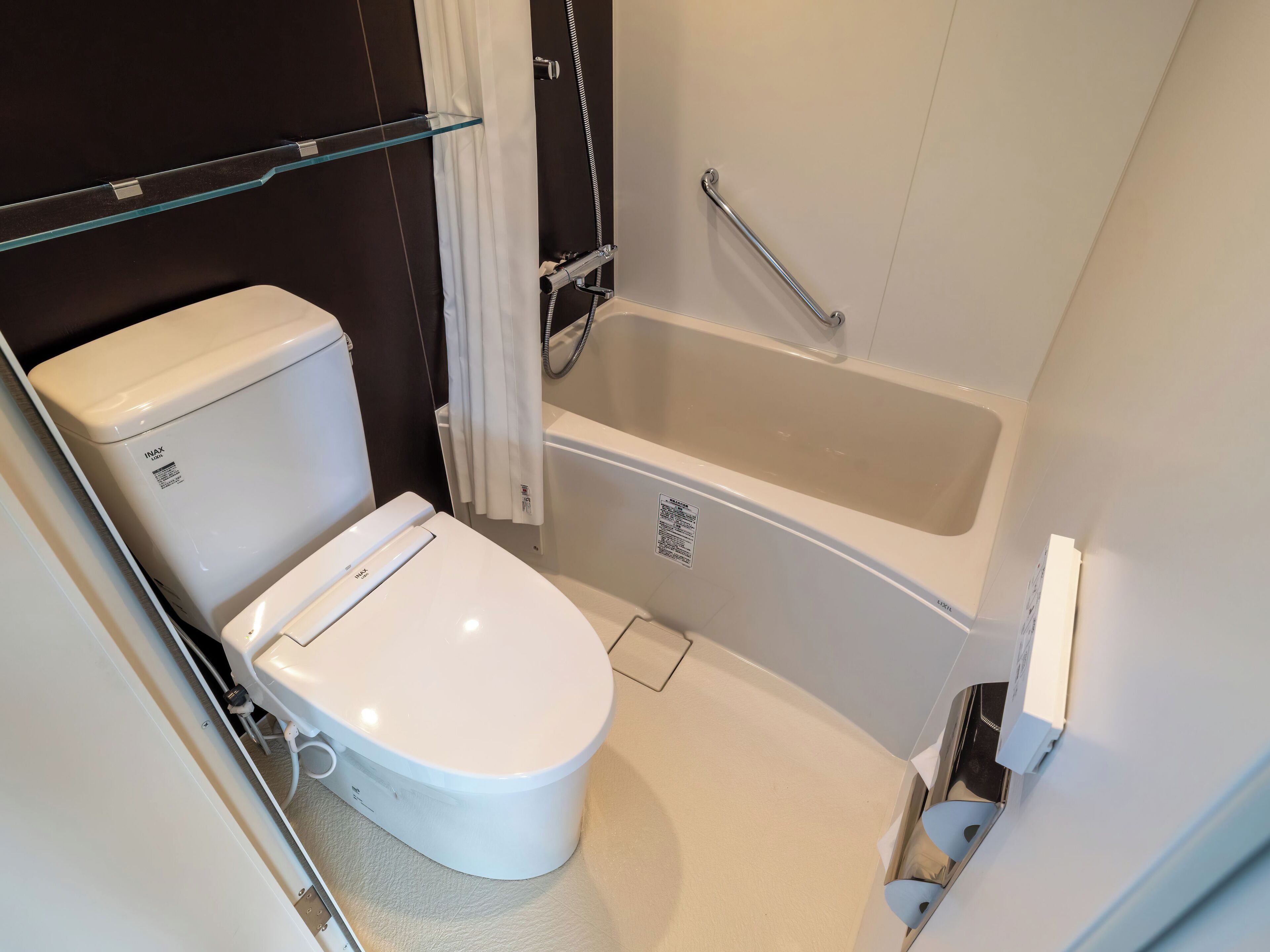 A small, modern bathroom with a toilet, a bathtub, and a glass shelf.