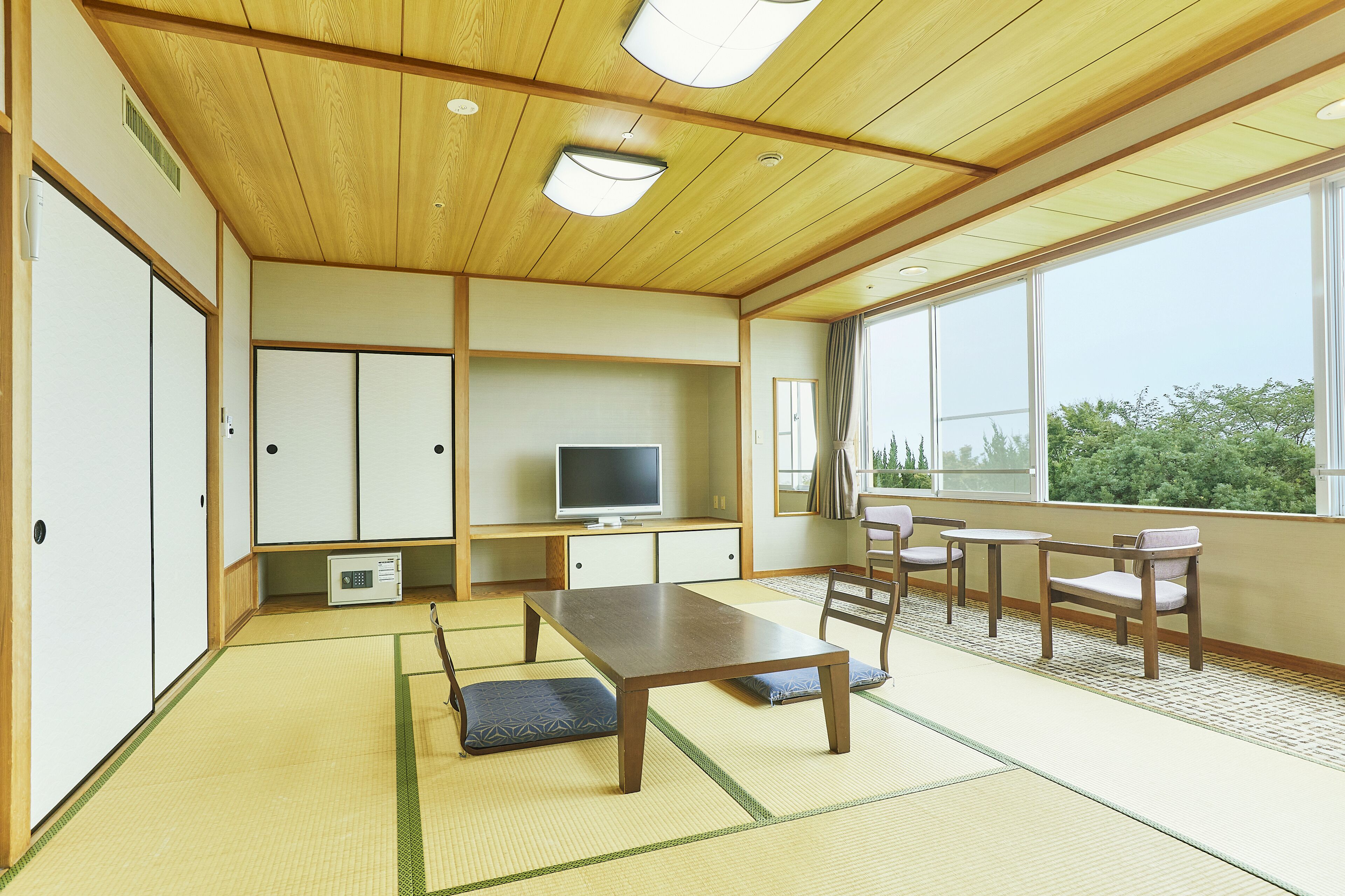 Una habitación japonesa tradicional con suelo de tatami, una mesa de madera baja y un televisor sobre un mueble.