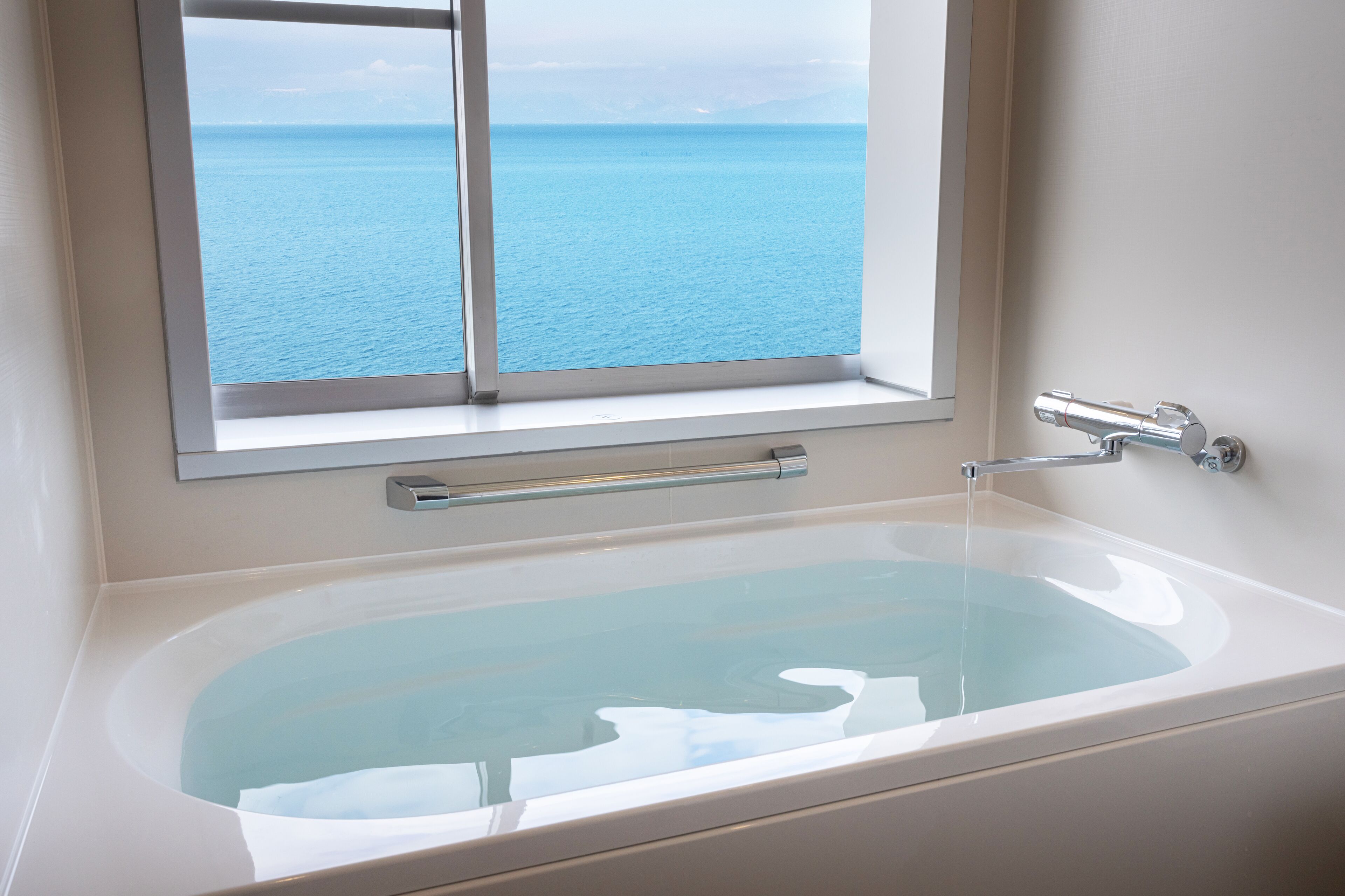 A bathtub with a view of the sea through a window.
