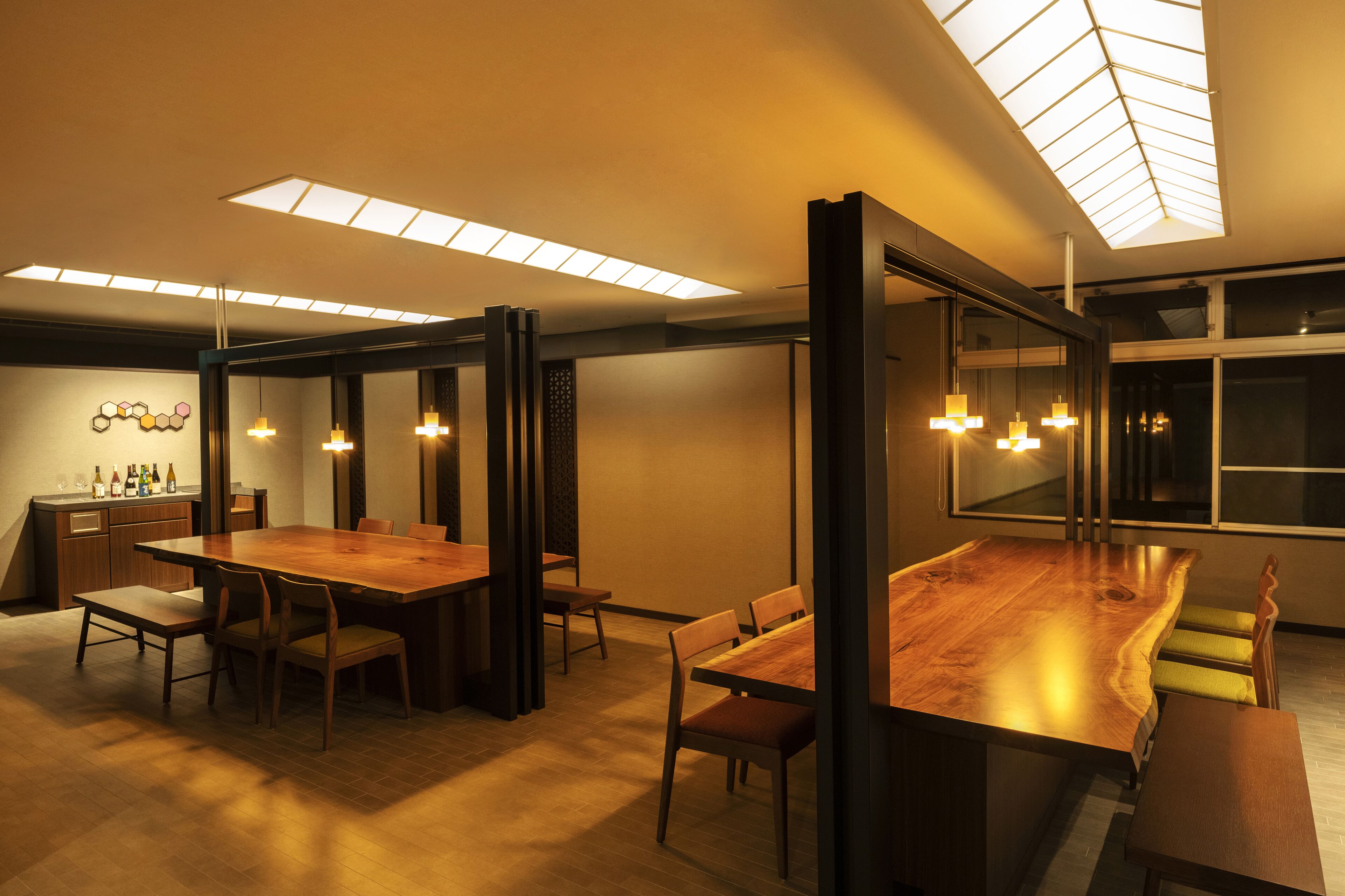 A modern dining area with a long wooden table, chairs, and pendant lighting.