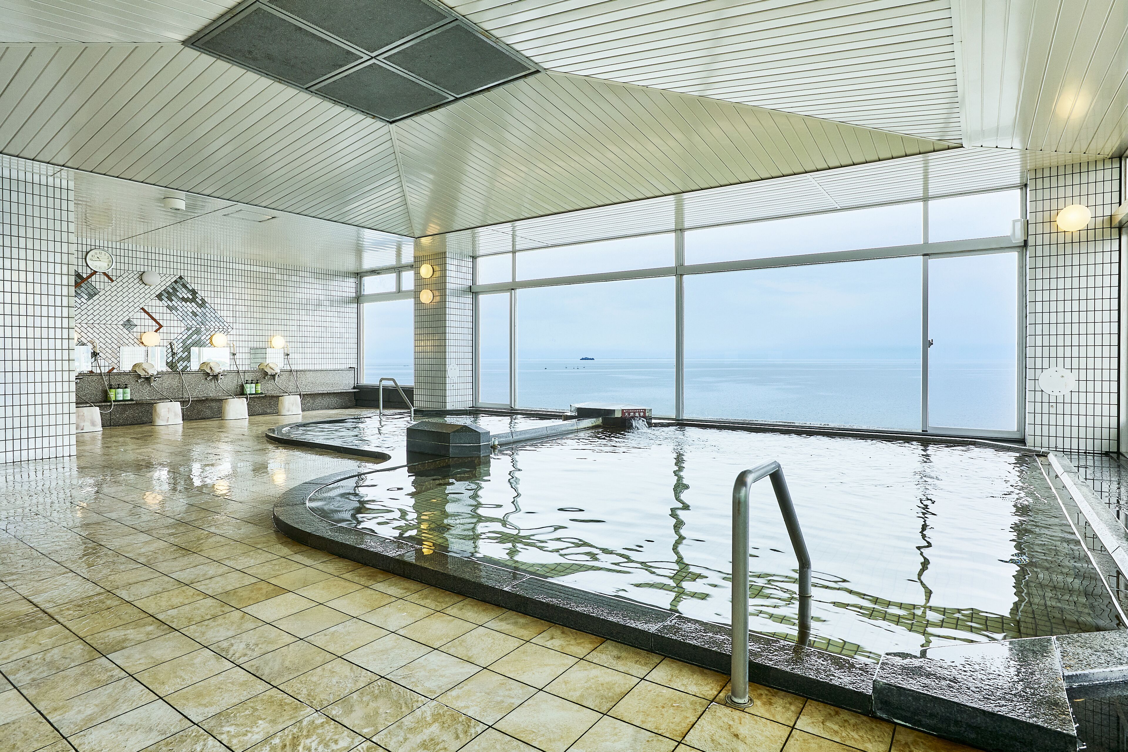 Piscina interior com vista para o mar, paredes revestidas com azulejos e teto com ventilação.