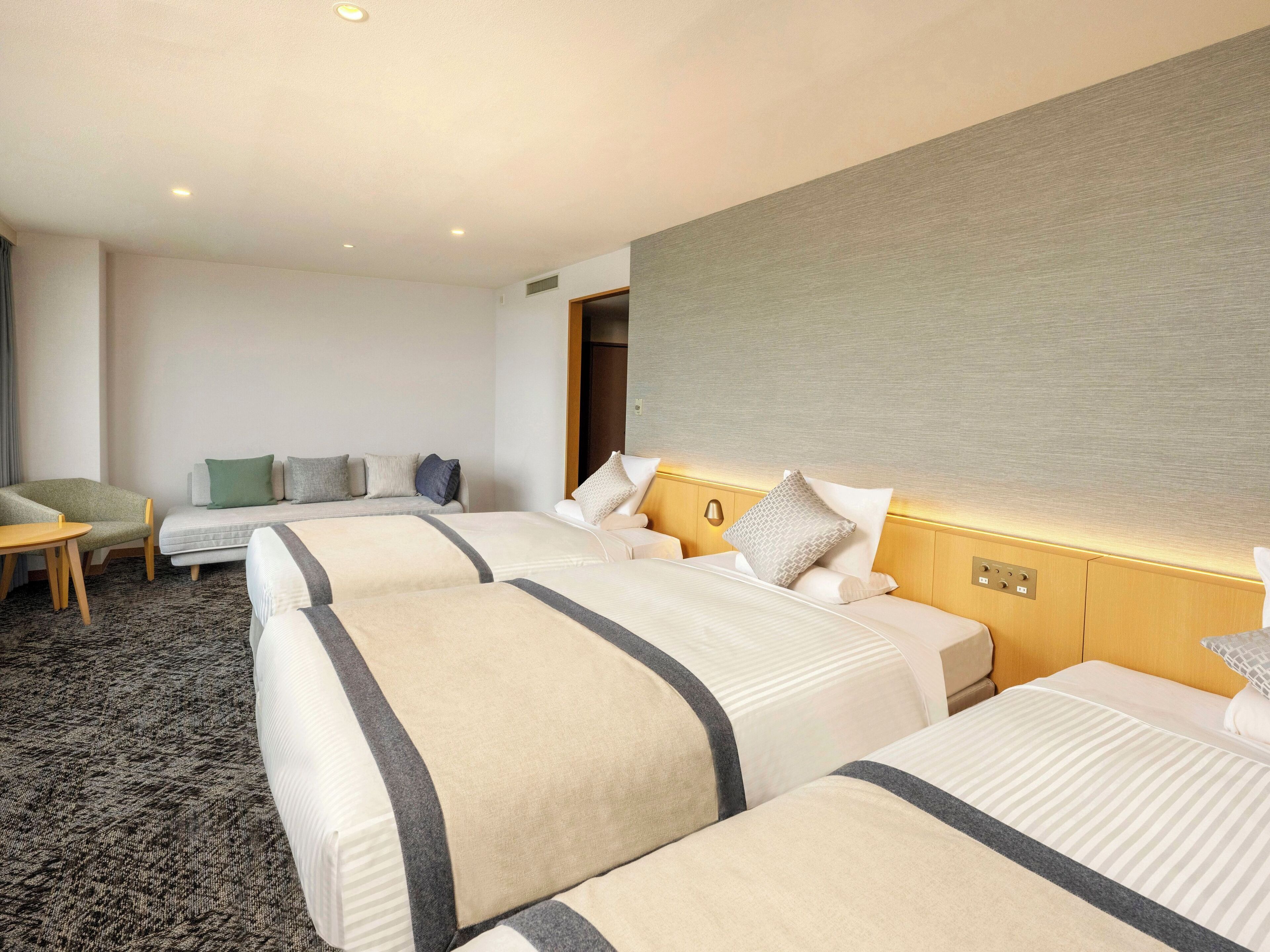 A hotel room with three beds, a sofa, a small table, and a carpeted floor.