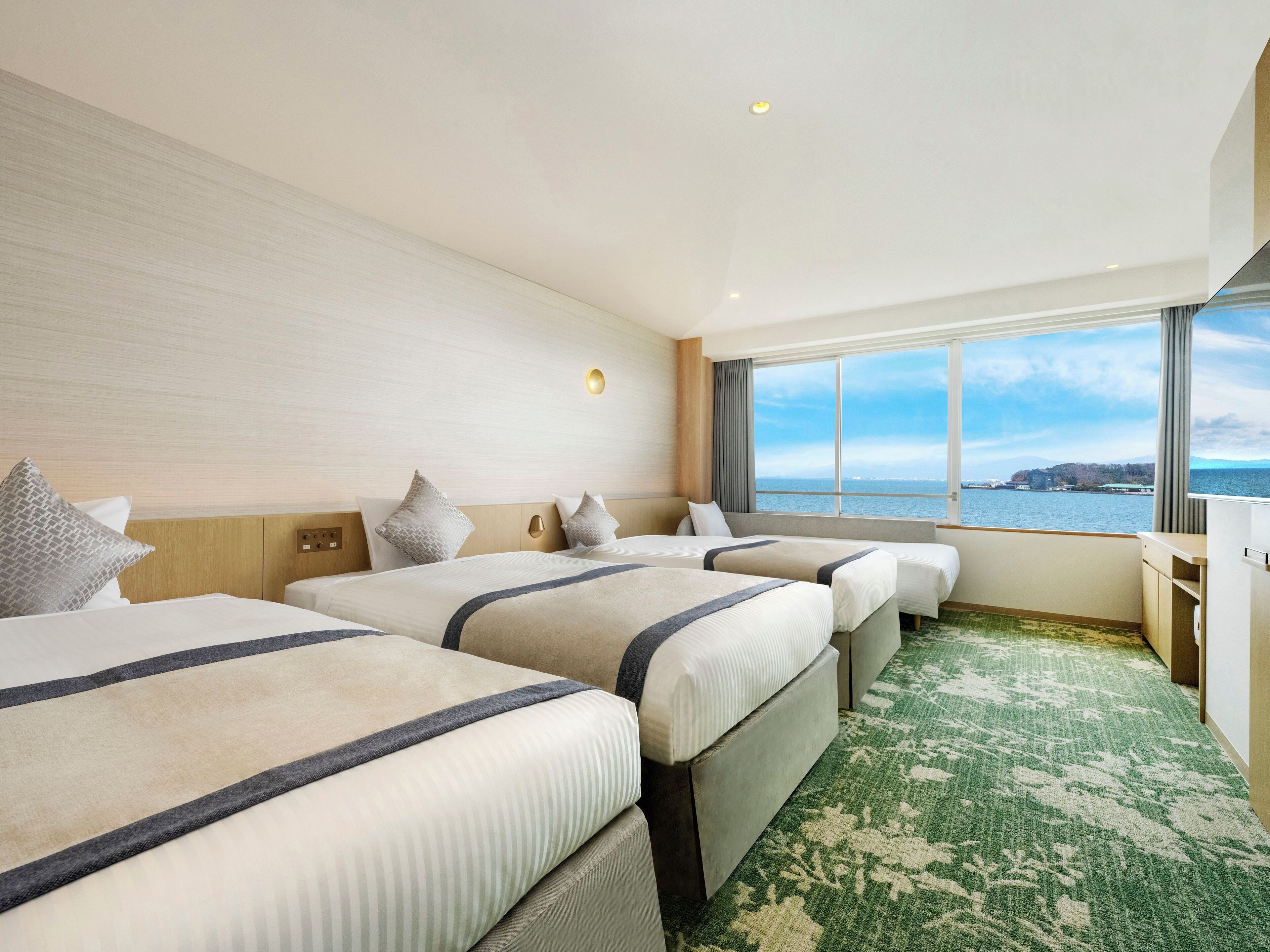 A hotel room with two beds, a large window with a view of the sea, and a green patterned carpet.