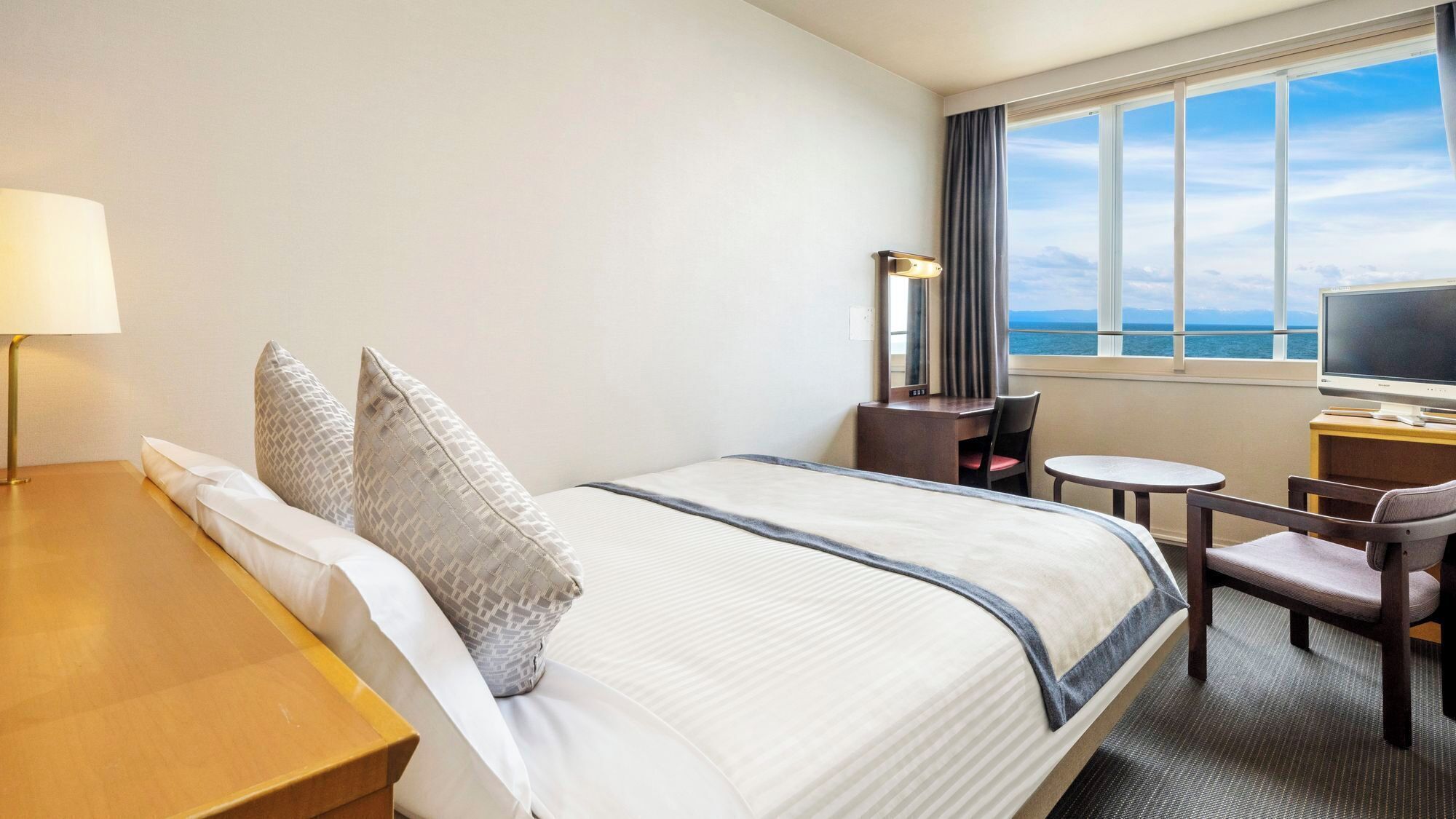 Une chambre d’hôtel équipée d’un lit, d’un bureau, d’une chaise, d’une télévision et d’une fenêtre donnant sur un paysage agréable.