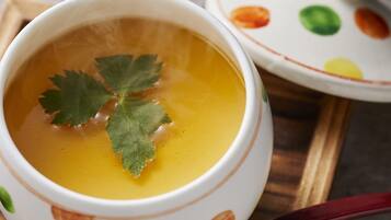 A bowl of soup with a leaf garnish, a spoon, and a patterned teapot on a tray.