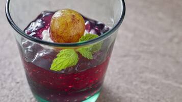 A glass with a red liquid, ice cubes, a fruit, and mint leaves.