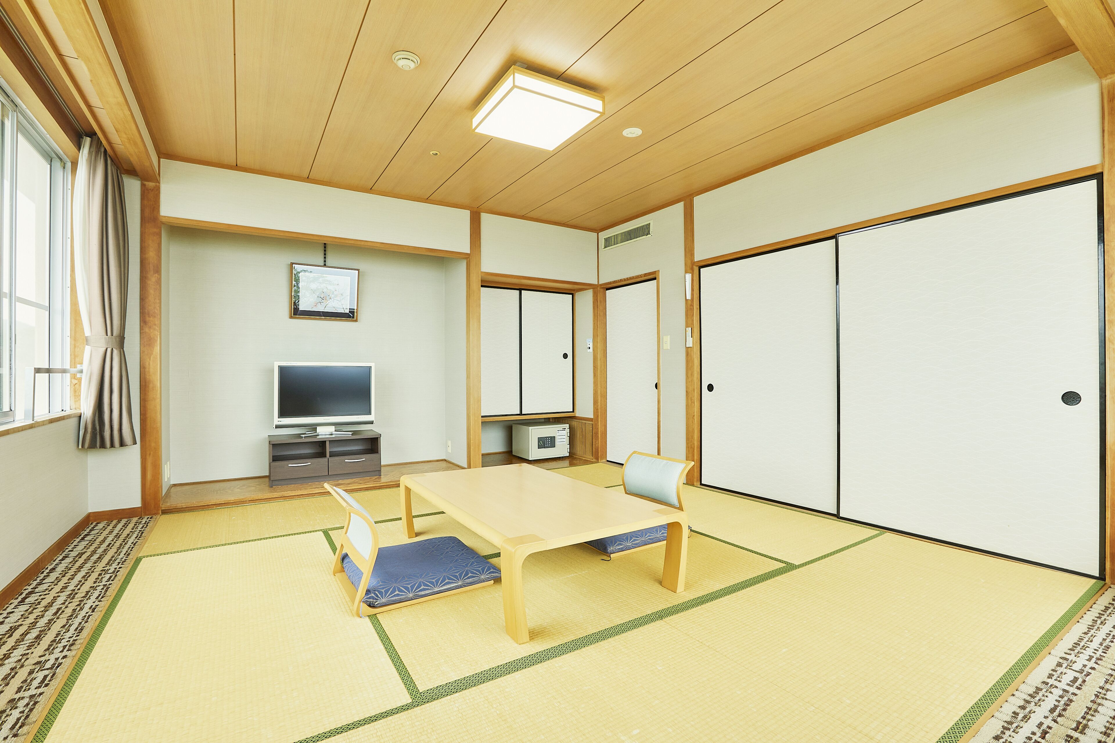 Une pièce de style japonais traditionnel, avec un sol recouvert de tatamis, une table basse, un téléviseur et des portes coulissantes.