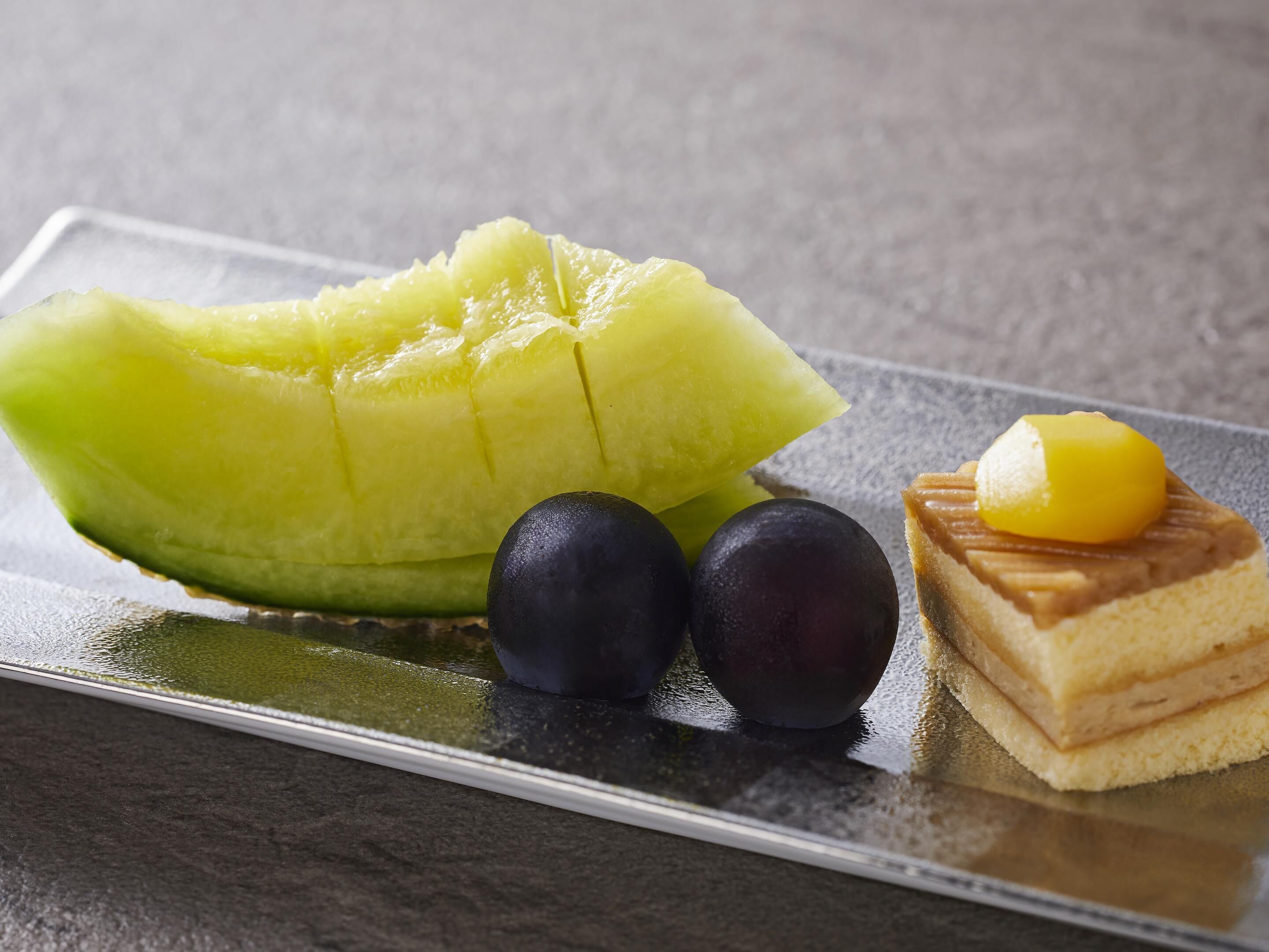 A plate with a slice of melon, two round fruits, and a dessert with a yellow topping.