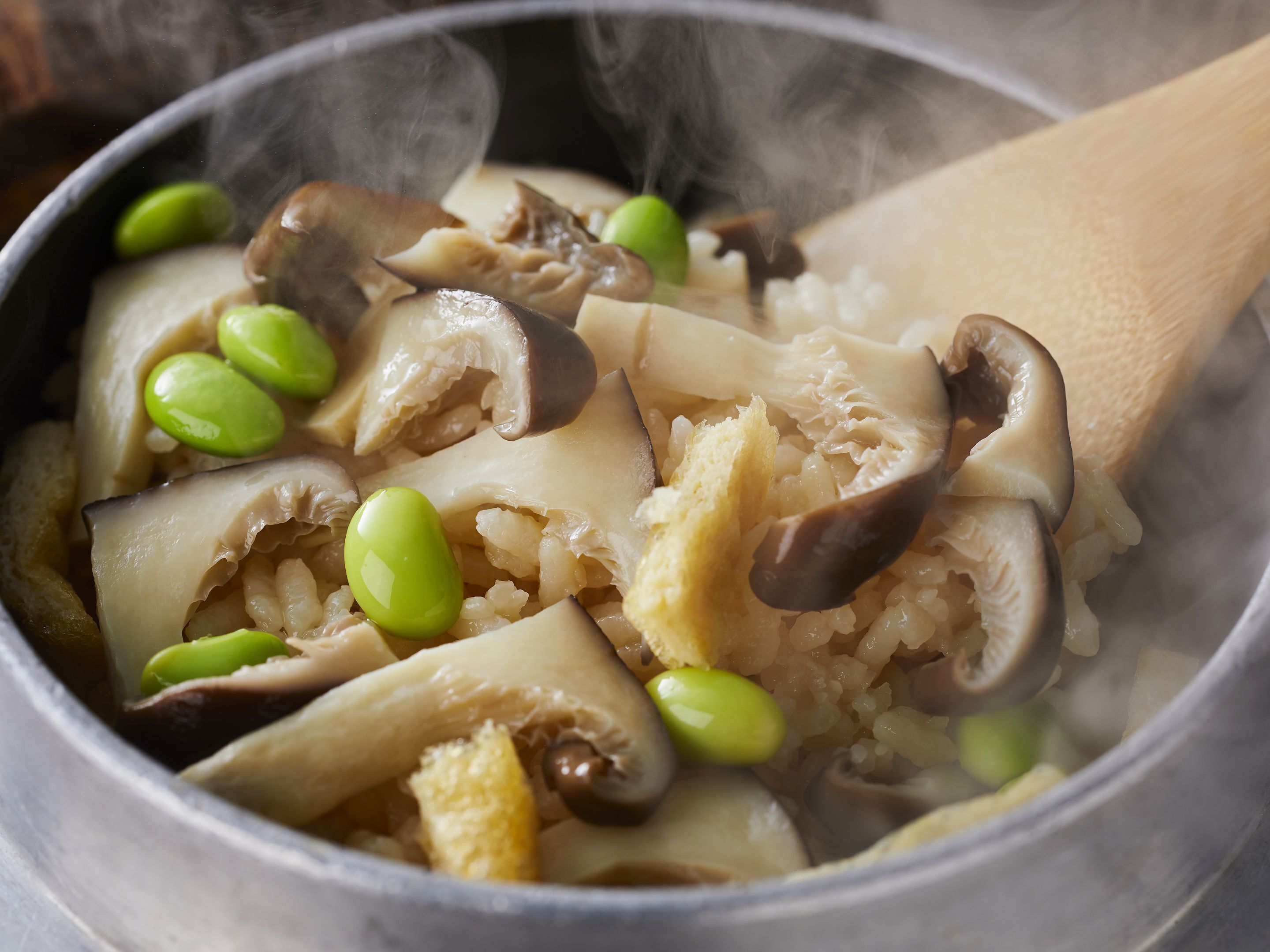 Eine Nahaufnahme eines Topfes mit Pilzen, Tofu und grünen Edamame-Schoten.