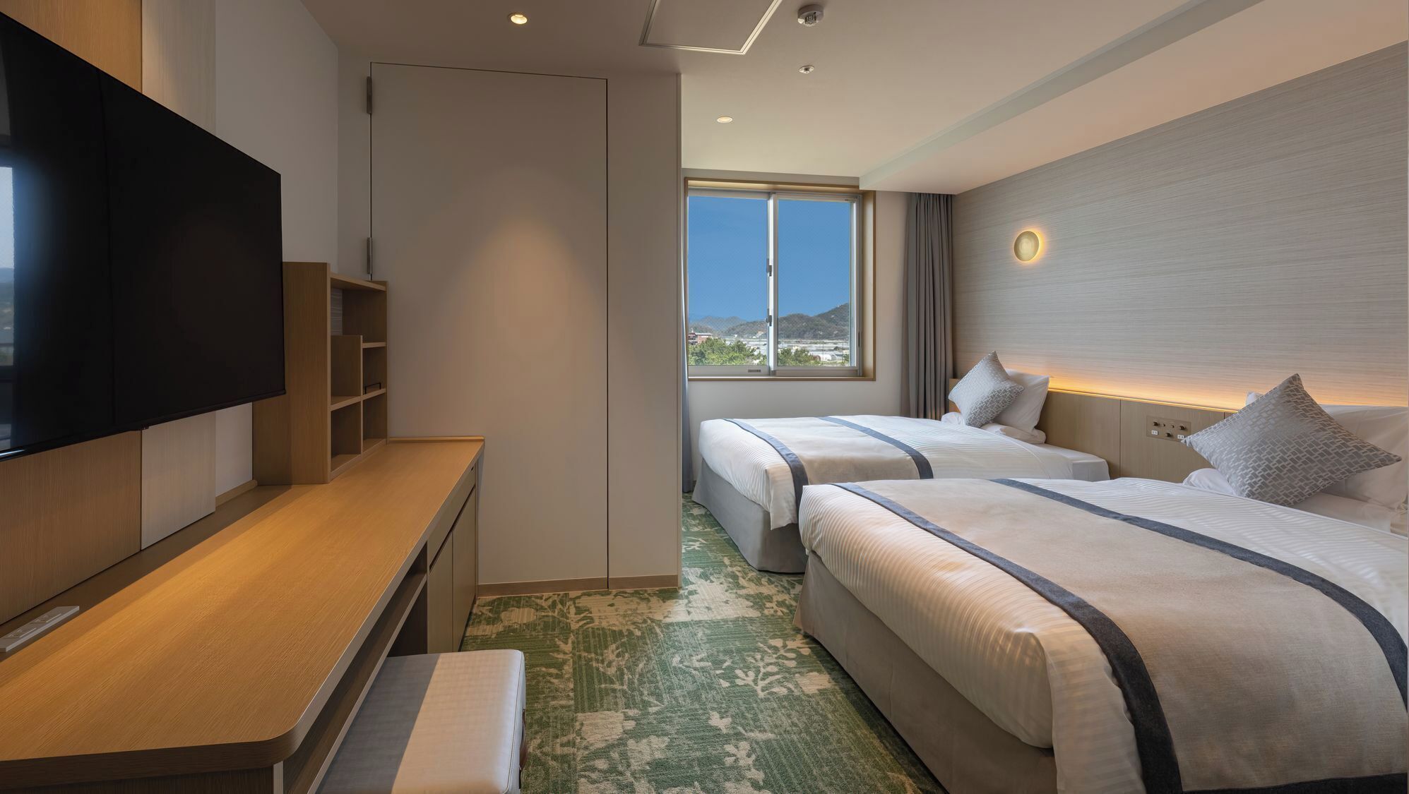 Une chambre d’hôtel équipée d’une télévision à écran plat, d’un bureau, de deux lits, d’une grande fenêtre et offrant une vue sur l’extérieur.