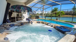 A hot tub with a view of a lake and palm trees, surrounded by a covered patio area. - Luxury 6BR / 3.5 Bathroom villa near Disney. Pool, Hot Tub, Games Room, etc. (Kissimmee)