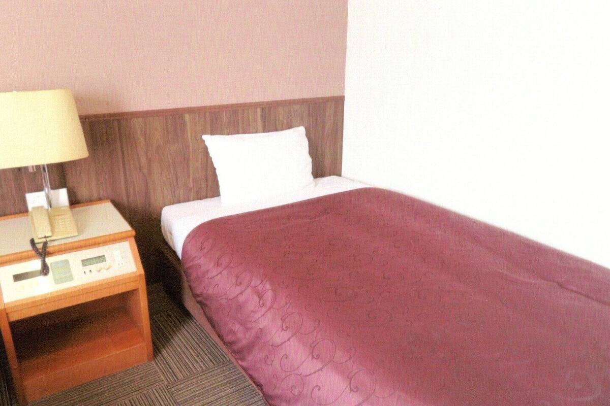 Una habitación de hotel con una cama individual, una mesita de noche con lámpara y un teléfono.