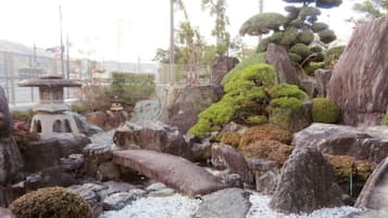 Un jardín ajardinado con formaciones rocosas, musgo y una pequeña pagoda.