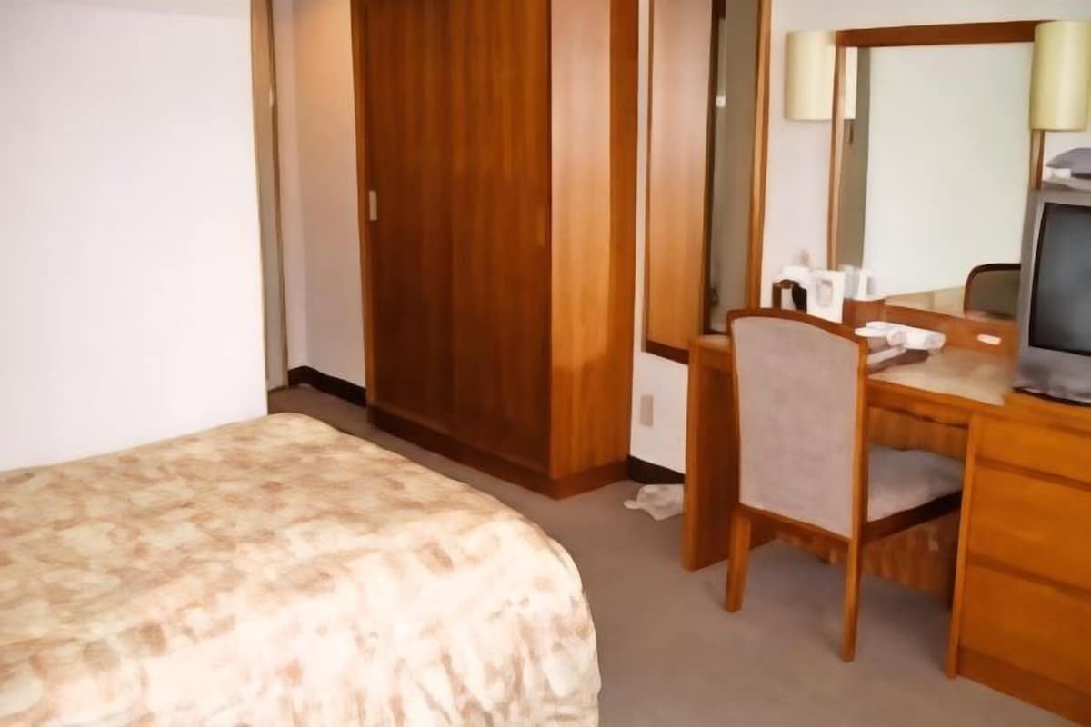 Una habitación de hotel con una cama, un escritorio de madera con una silla, un espejo y un televisor.