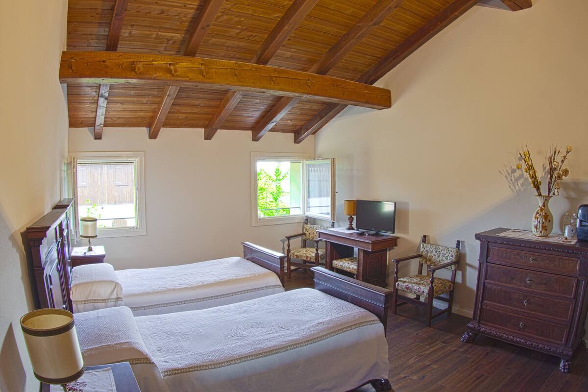 Ein Schlafzimmer mit zwei Betten, Holzboden, Schreibtisch mit Stuhl, Kommode und Fernseher.