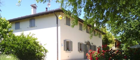 A two-story building with a white facade, multiple windows with shutters, and a visible satellite dish.