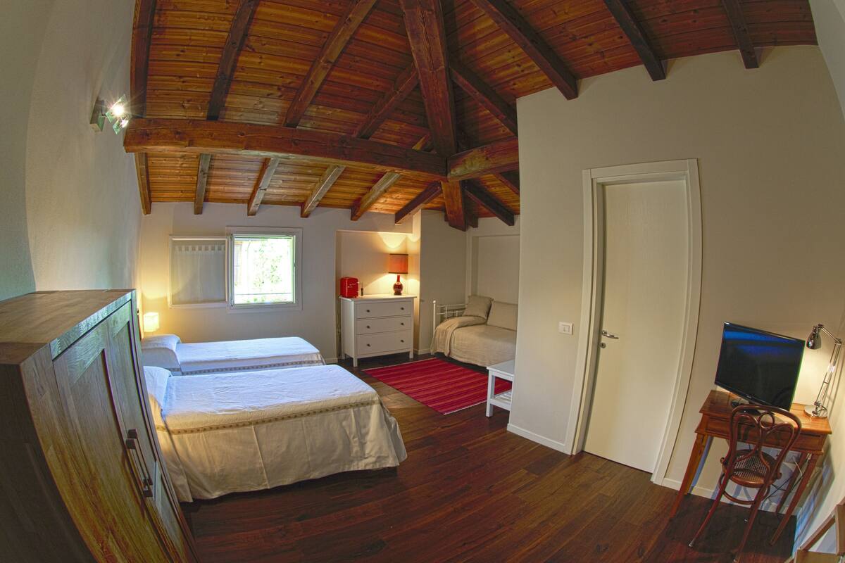 Ein Schlafzimmer mit zwei Betten, einem Schreibtisch mit Computer, einem Stuhl, einem roten Teppich und einer Holzbodenverkleidung.